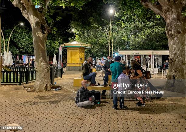 Group of young people sitting on a bench, singing after midnight in the Alameda de Hercules on May 15, 2021 in Seville, Andalusia.