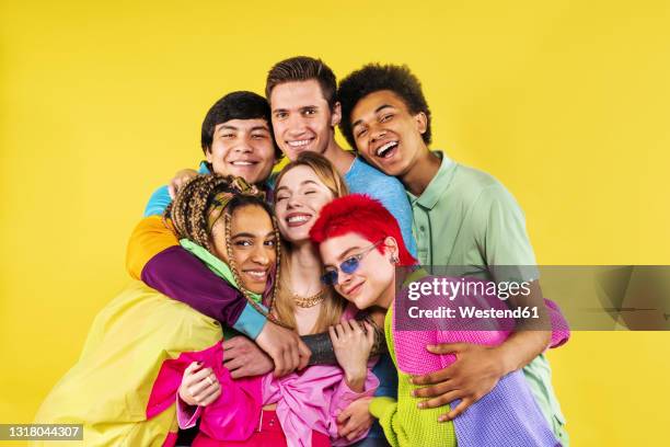 young friends embracing each other while standing in front of yellow background - embracing differences stock pictures, royalty-free photos & images