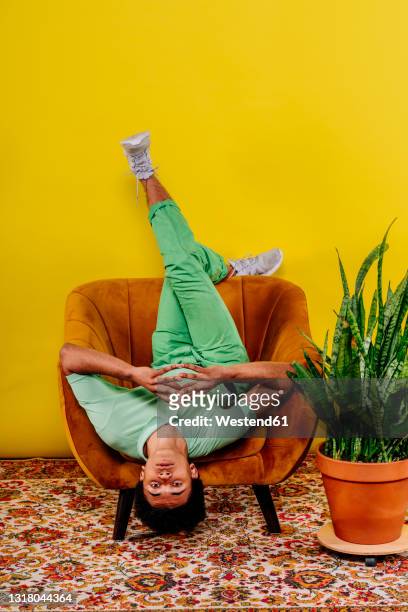 man sitting upside down on armchair in studio - voeten omhoog stockfoto's en -beelden