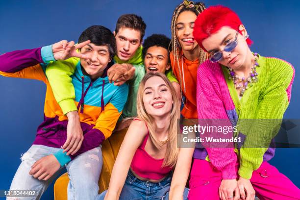 smiling friends sitting together in front of blue background - vestito multicolore foto e immagini stock