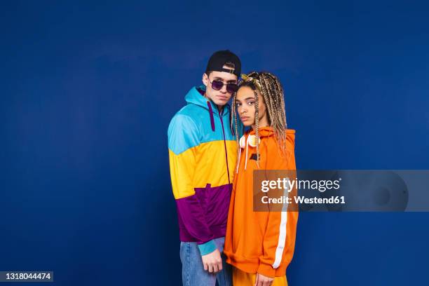 friends wearing hooded shirt staring while standing together by blue background - couples studio portrait stock-fotos und bilder