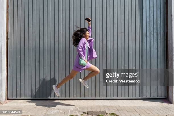 excited woman jumping by gray wall - saltare foto e immagini stock