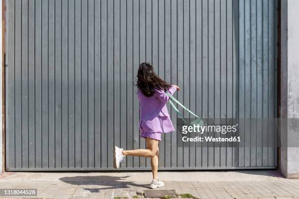 mid adult woman dancing in front of gray wall - lila handtasche stock-fotos und bilder