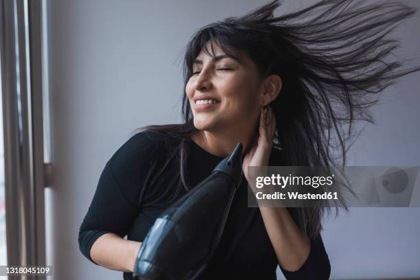 mid adult woman drying hair through hair dryer at home - haare föhnen stock-fotos und bilder