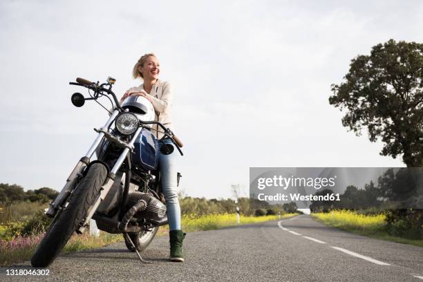 smiling female biker looking away while sitting on motorcycle - woman motorcycle stock pictures, royalty-free photos & images