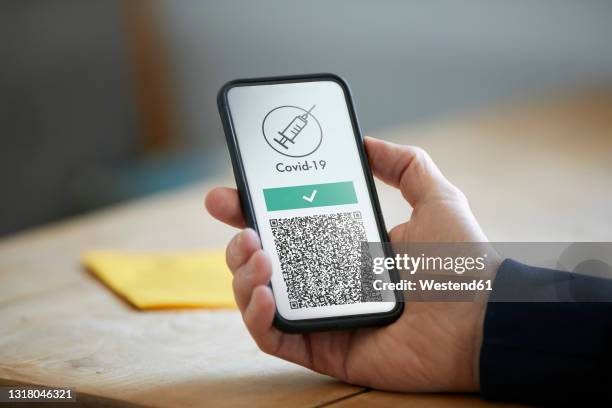 man holding smart phone with covid-19 vaccination qr code - immunisation certificate stock-fotos und bilder