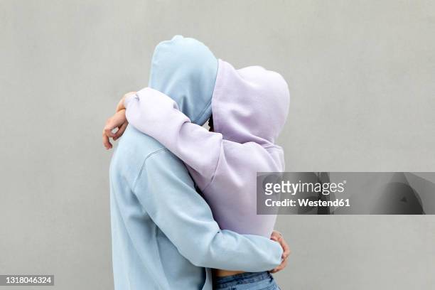 couple in hooded shirt embracing each other by wall - boy hug males stock-fotos und bilder