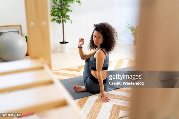 woman with curly hair doing spinal twist pose at home - spinal twist stock pictures, royalty-free photos & images