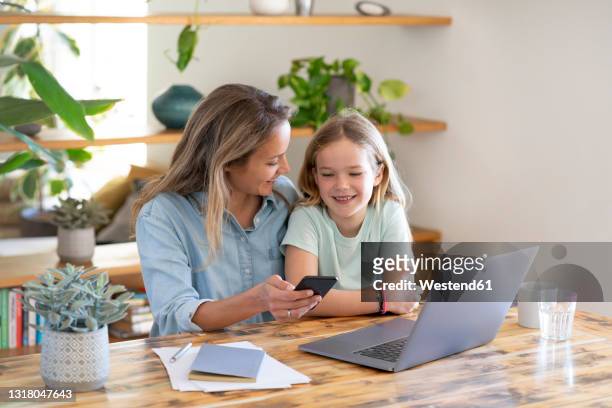 businesswoman and daughter sitting with laptop and smart phone at table - freelance child stock-fotos und bilder