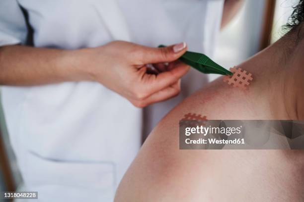 female physical therapist sticking eleastic cross tape through tweezer on patient's shoulder in clinic - kinesiotape stock pictures, royalty-free photos & images