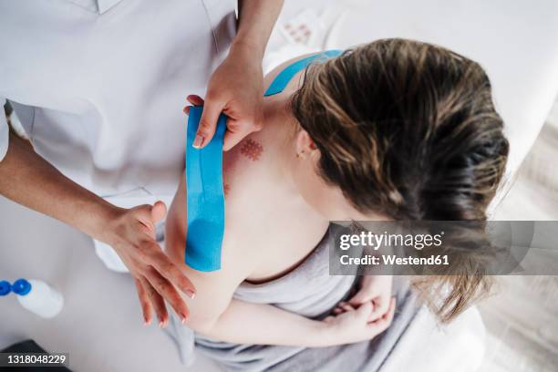female physical therapist sticking elastic therapeutic tape to patient's shoulder in clinic - kinesiotape stock pictures, royalty-free photos & images