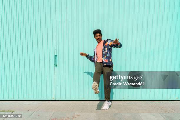 man dancing in front of of turquoise wall during sunny day - dar uma ajuda imagens e fotografias de stock