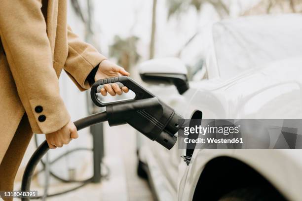 woman charging electric car at station - electric car charging stock pictures, royalty-free photos & images