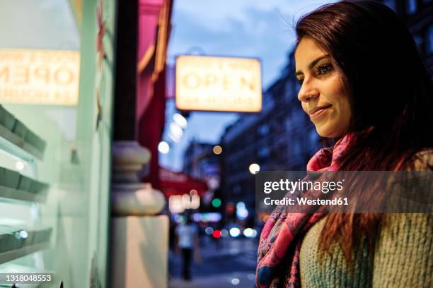 smiling woman looking at store display in city - soho london night stock pictures, royalty-free photos & images