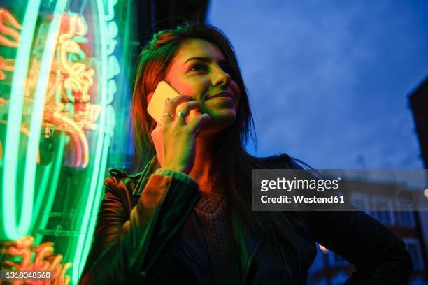smiling woman using mobile phone by standing illuminated light - tourist talking on the phone stock pictures, royalty-free photos & images