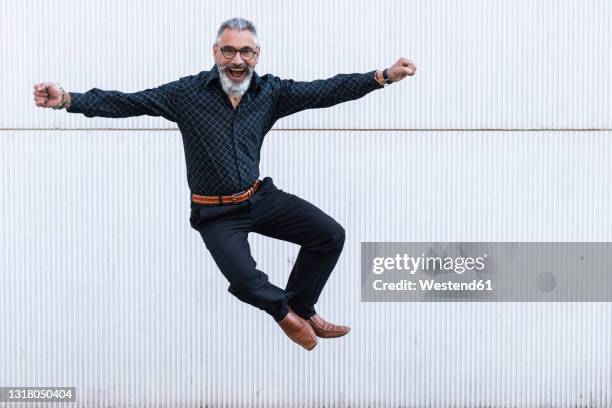 carefree man with arms outstretched jumping in front of wall - erwachsene im geschäft in höherer position stock-fotos und bilder