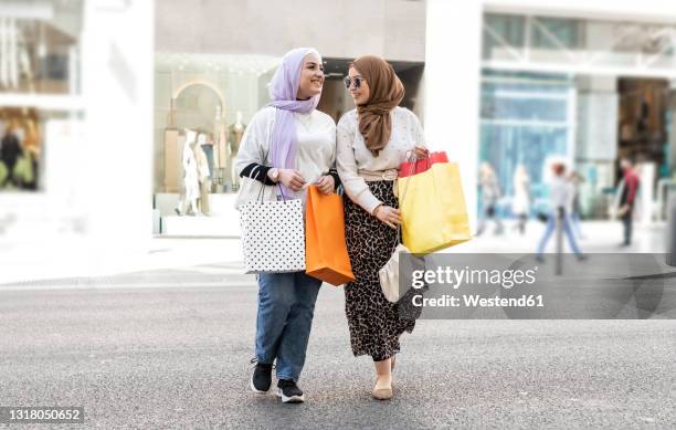 female arab friends crossing road while shopping in city - arab shopping stockfoto's en -beelden
