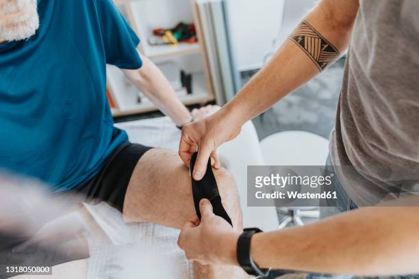 male physiotherapist sticking elastic therapeutic tape on knee of patient - kinesiotape stock pictures, royalty-free photos & images