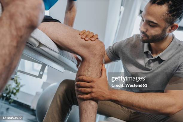 male physical therapist examining knee of patient in practice - fysiotherapeut stockfoto's en -beelden