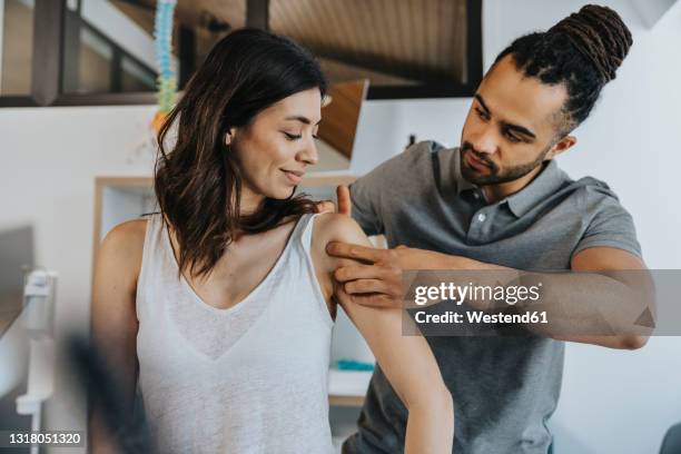 physiotherapist examining shoulder of female patient in practice - fisioterapia fotografías e imágenes de stock