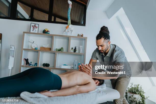 female patient receiving spine massage in medical practice - black massage therapist fotografías e imágenes de stock