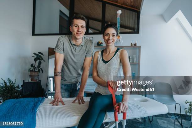 young physiotherapist with smiling female patient holding crutch in medical practice - krücken stock-fotos und bilder