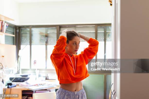 young woman wearing orange crop top looking in mirror at home - bauchfreies oberteil stock-fotos und bilder