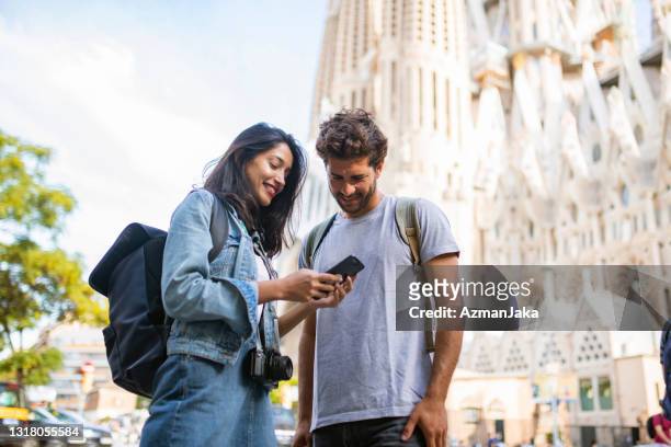 young tourist couple looking at smart phone in barcelona - looking to the camera imagens e fotografias de stock