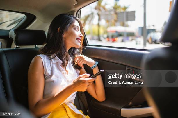 young female vacationer with smart phone in backseat of taxi - indian ethnicity car stock pictures, royalty-free photos & images