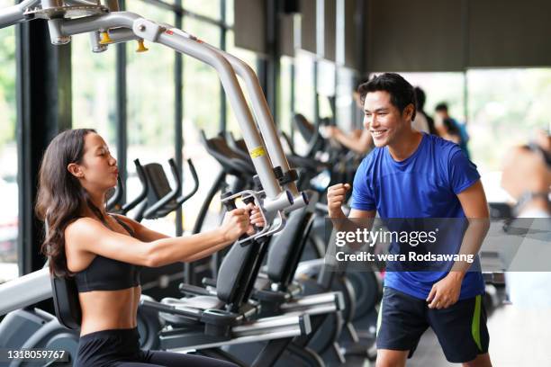 personal trainer guiding young woman to lifting weights at gym - フィットネスマシン ストックフォトと画像