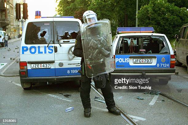 Riotpolice officer guards vehicles damaged by anti-capitalist demonstrators June 15, 2001 in Gothenberg, Sweden as fighting breaks out at a...