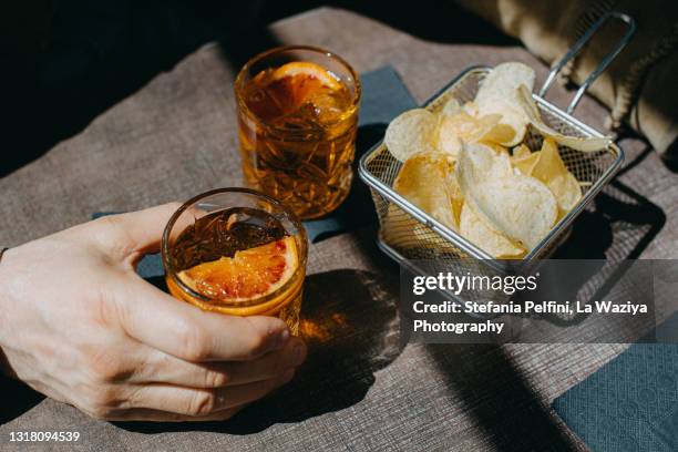 man's hand holding a glass of crodino/aperol/spritz - cocktail and mocktail stockfoto's en -beelden