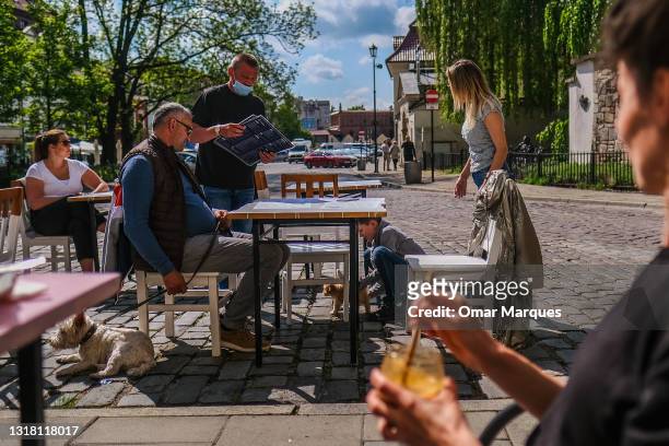 Waiter wears a protective face mask as he attends to clients orders on the Jewish district on May 15, 2021 in Krakow, Poland. Bars and restaurants...