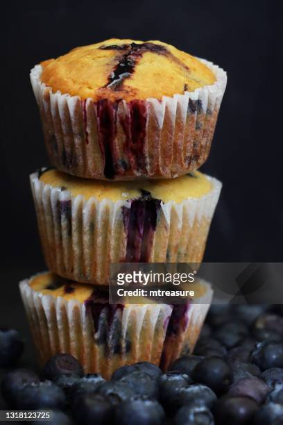 image of stack homemade blueberry muffins in paper cake cases surrounded by fresh blueberries, black background, focus on foreground - cupcake holder stock pictures, royalty-free photos & images