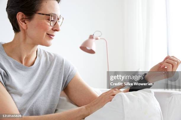 Woman In Her 40s Sitting On A Sofa And Measuring Her Blood Pressure, Stock-Foto