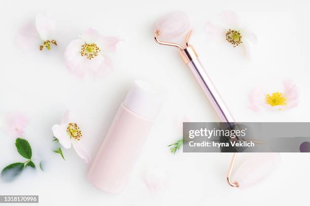 beautiful white rose flowers and cleansing milk or serum in a pink vial, rose quartz facial roller in milk bath. - white rose flower spa stock-fotos und bilder