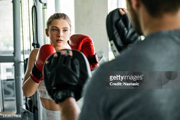 young woman sparring with a boxing trainer at the gym - kickboxing training stock pictures, royalty-free photos & images