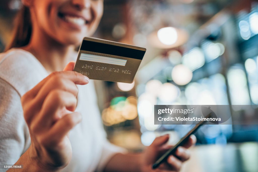Frau mit Smartphone und Kreditkarte für Online-Shopping in Stadtcafé.