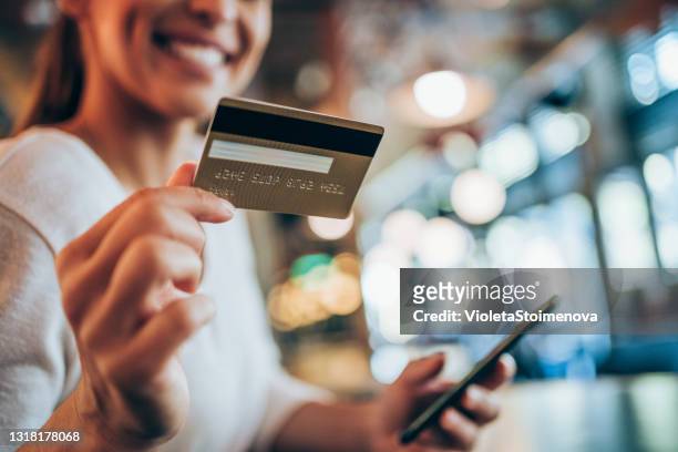 woman using smart phone and credit card for online shopping in city cafe. - credit card stock pictures, royalty-free photos & images