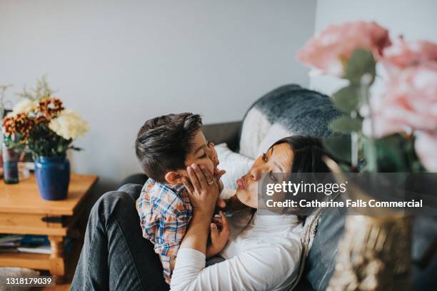 mother and son mess about on a sofa together - knees together - fotografias e filmes do acervo