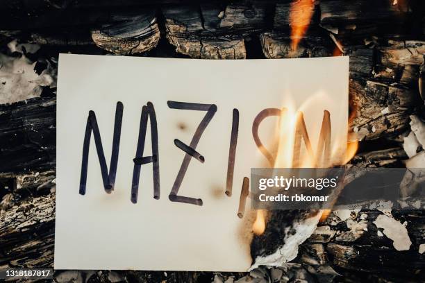 the word nazism on white paper burning in a flame of fire - nazi swastika stock pictures, royalty-free photos & images