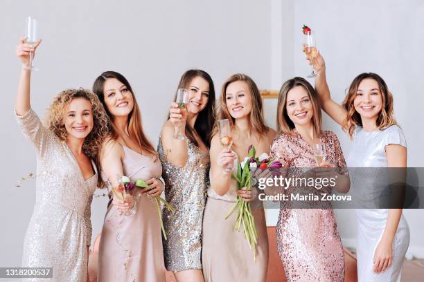 a group of beautiful women in dresses smile, celebrate and raise a toast and have fun together. girls ' party - bruidsmeisje stockfoto's en -beelden