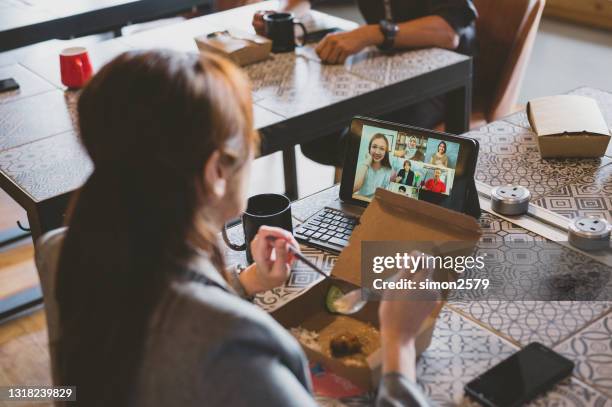 an asian young businesswoman having her packed lunch meal while video call with her customer in cow-office space - virtual lunch stock pictures, royalty-free photos & images