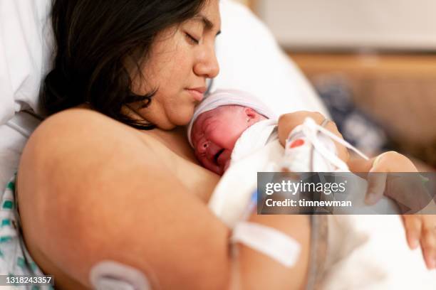 mother holding brand new baby in hospital delivery room - childbirth stock pictures, royalty-free photos & images