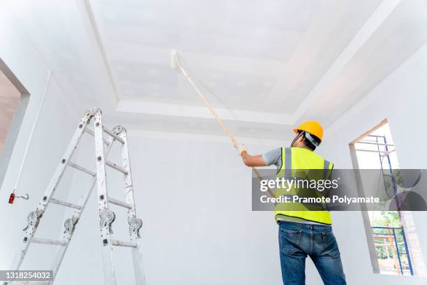 rear view of asian painter man painting the wall, with paint roller and bucket in an unfinished house, construction work, isolated on big empty space with ladder - dipinto foto e immagini stock