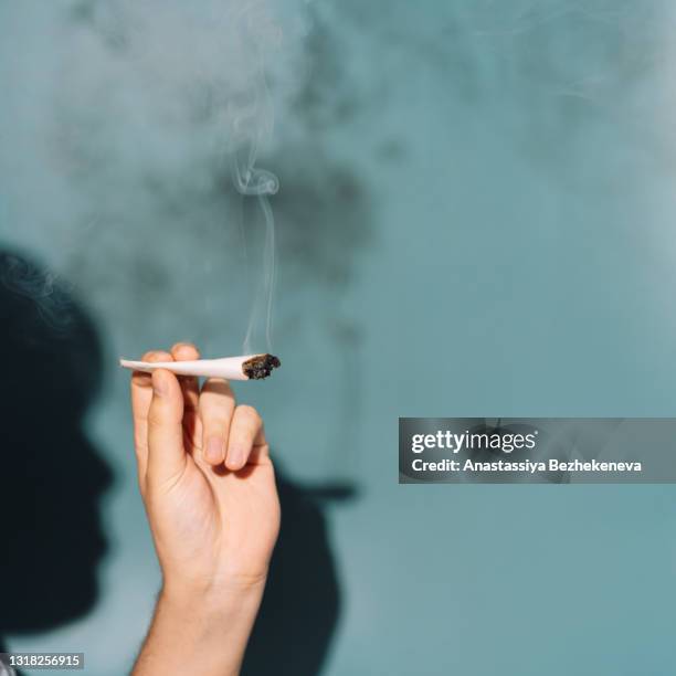 lit cigarette in hand against green background - hash-joint stock pictures, royalty-free photos & images