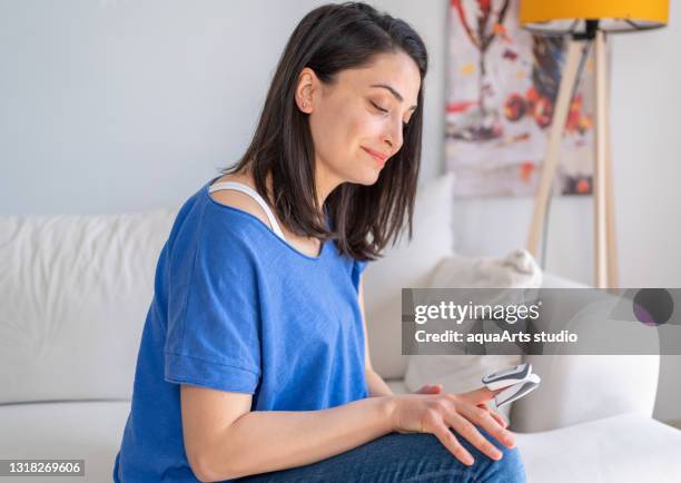 woman is measuring, monitoring oxygen saturation with digital pulse oximeter at home. woman with coronavirus, covid-19 pandemia quarantine lockdown.  digital pulse oximeter at home to test oxygen level in blood and pulse rate. - saturated color stock pictures, royalty-free photos & images