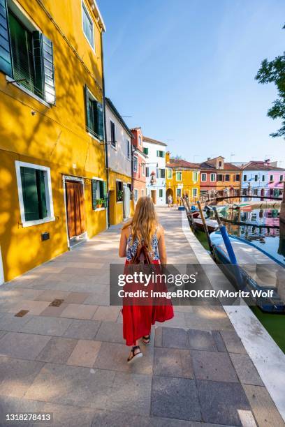young woman in front of colorful houses, canal with boats and colorful house facades, burano island, venice, veneto, italy - burano foto e immagini stock