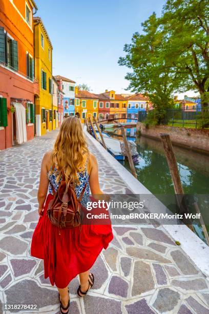 young woman in front of colorful houses, canal with boats and colorful house facades, burano island, venice, veneto, italy - burano foto e immagini stock