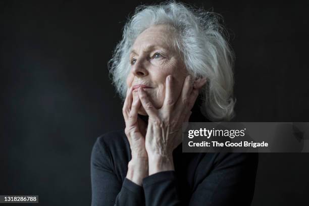 portrait of thoughtful senior woman holding head in hands - body part black background stock pictures, royalty-free photos & images